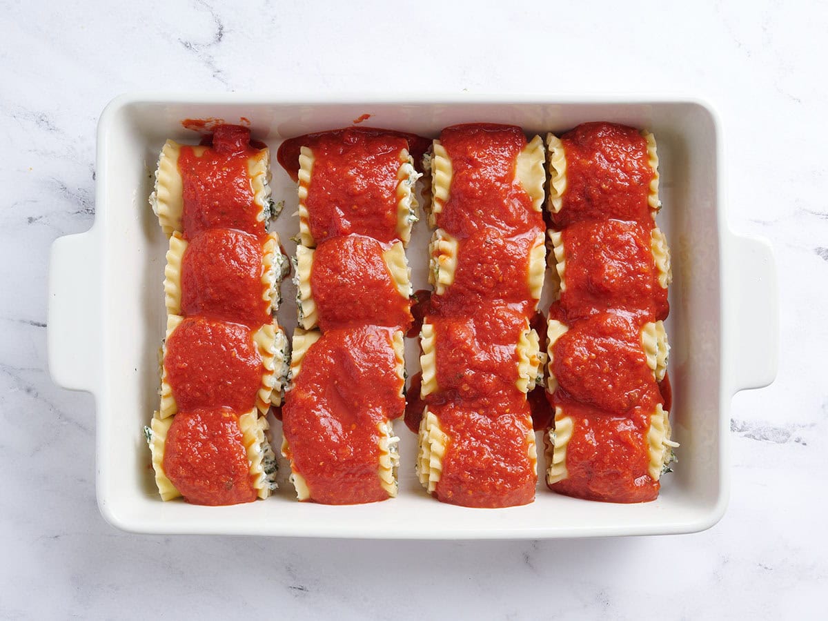 Lasagna roll ups in a baking dish covered in sauce.