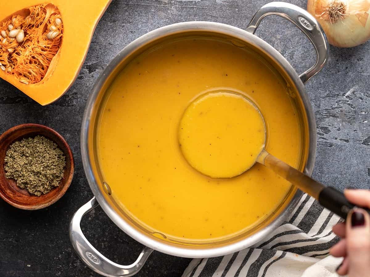Overhead view of a pot full of butternut squash soup with the ladle being lifted.