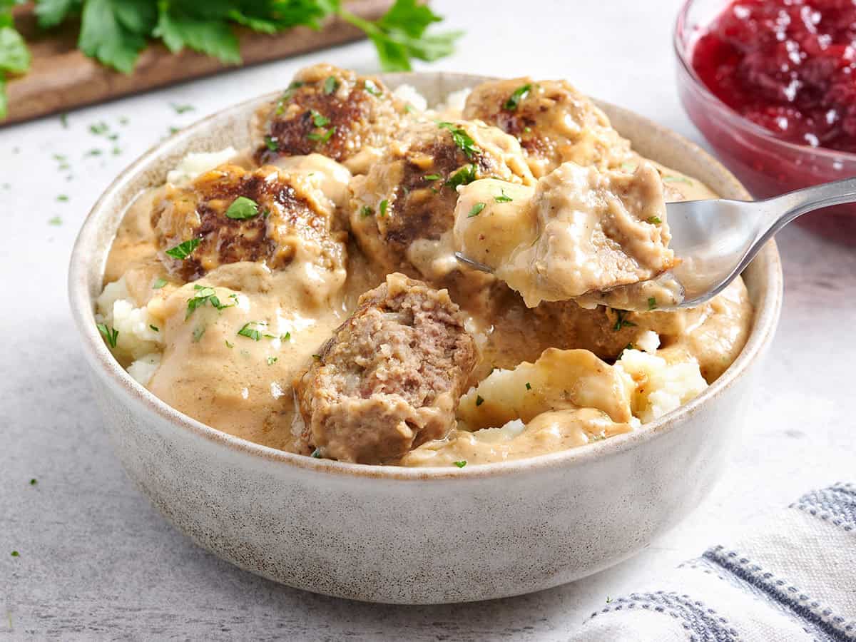 Side view of a bowl of Swedish meatballs with mashed potatoes and a fork taking some.
