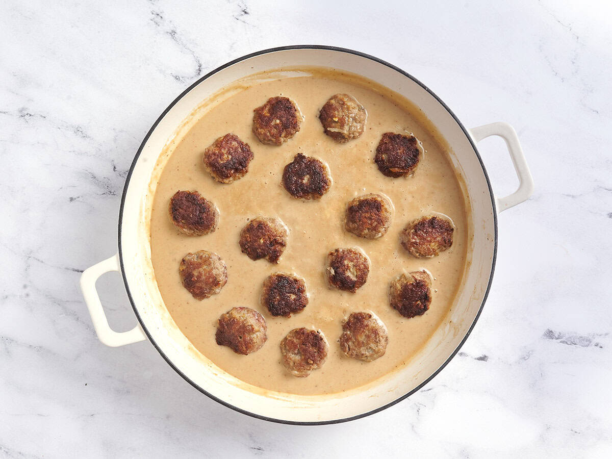 Swedish meatballs added to a creamy sauce in a pot.