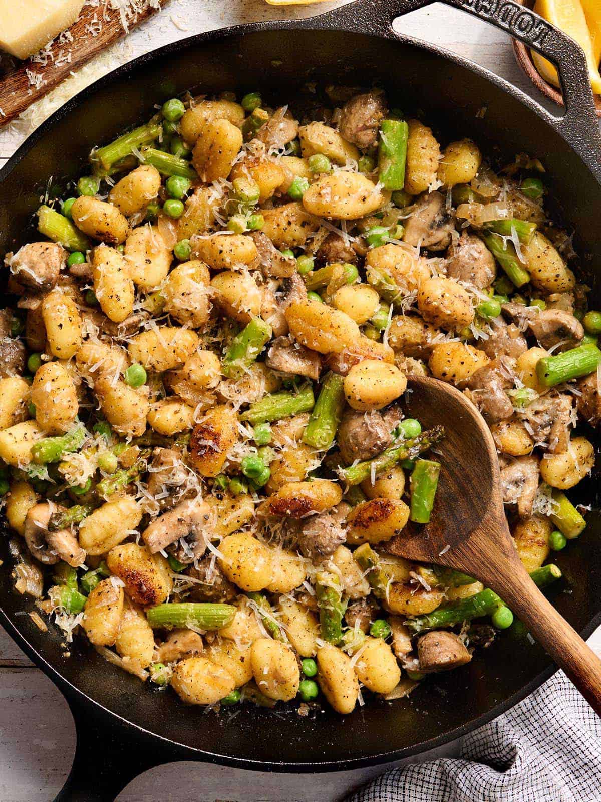 Overhead view of gnocchi with spring vegetables in a skillet with a wooden spoon.