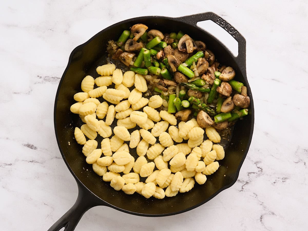 Gnocchi added to a skillet with asparagus and mushrooms.