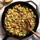 Overhead view of gnocchi with spring vegetables in a skillet with a wooden spoon.