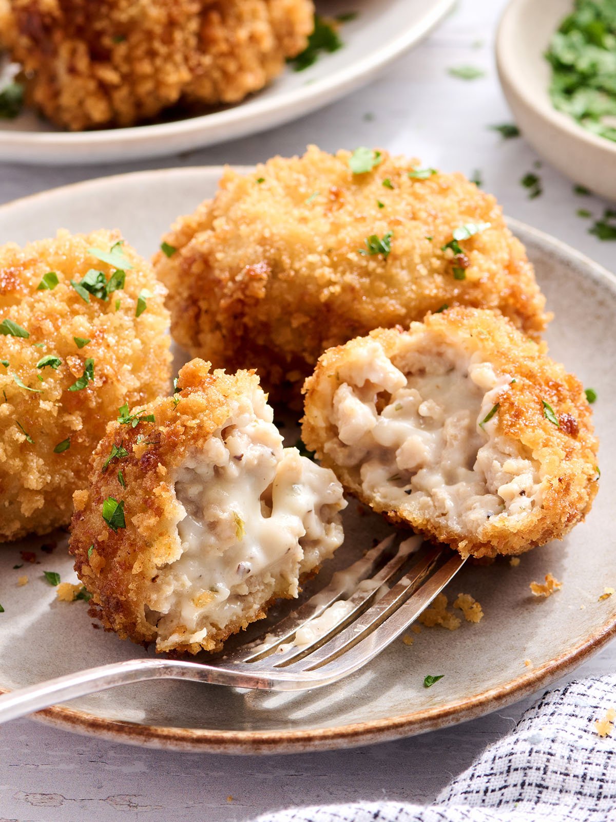 Side view of chicken croquettes on a plate with one sliced in half.