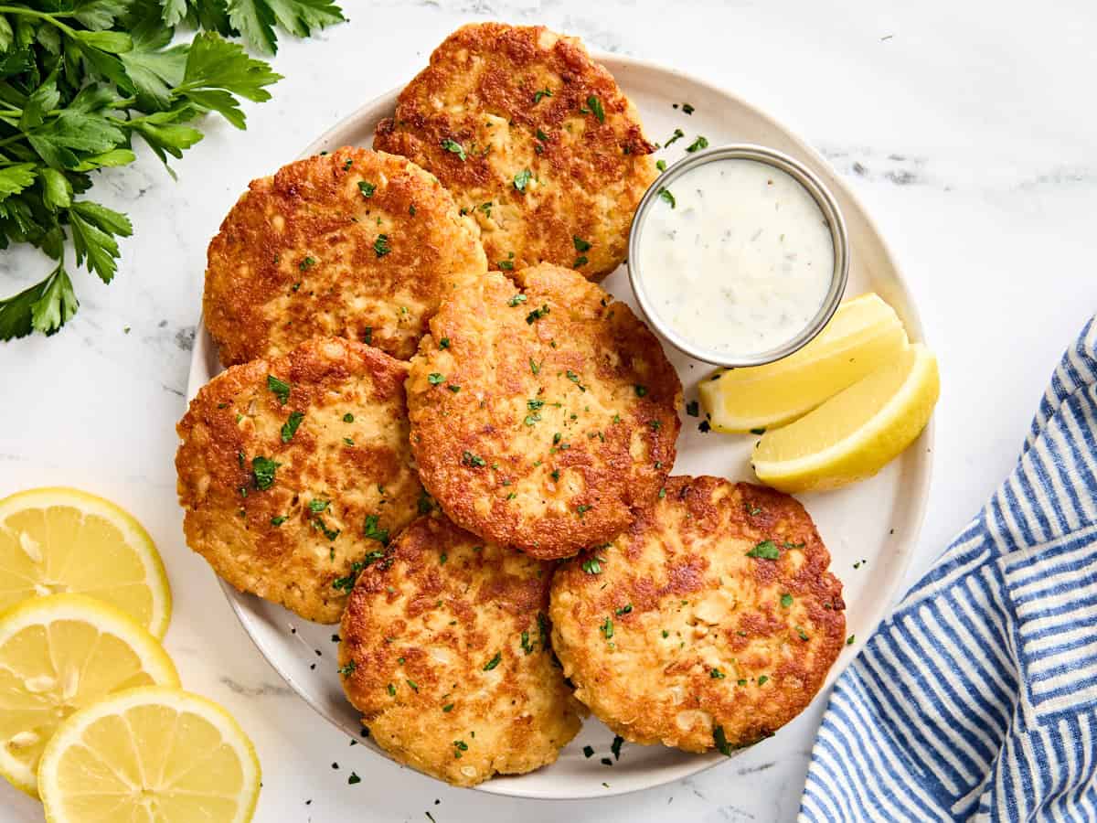 Overhead view of homemade salmon patties on a plate with tartar sauce and lemon wedges.