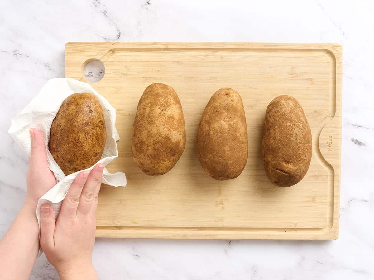 Potatoes on a cutting board being dried with a paper towel.