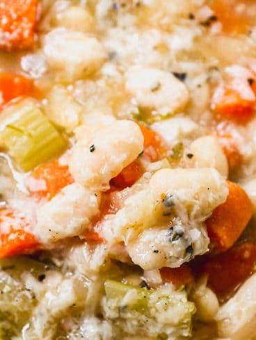 A close-up of a bowl of vegetable and bean soup with carrots, celery, and white beans in a broth.