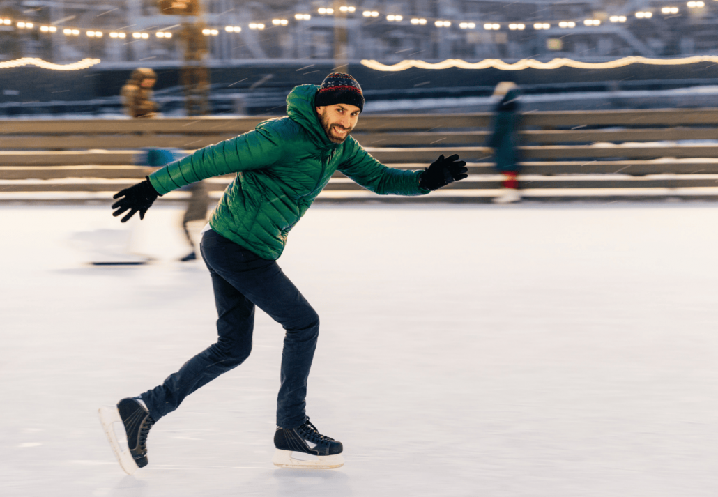 Cheerful male has fun outdoor, skates on ice ring, enjoys this winter activity, moves actively